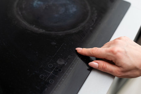 Close up of electric stove control panel, male finger pressing buttons, red LED indicators switched onの写真素材