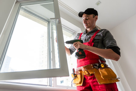 Professional installer of plastic windows poses in a working uniform, holds glasses with his hand. Specialist in the installation of plastic windows looks into the camera with a serious lookの写真素材