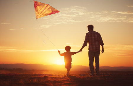 Portrait of father and child together in sunset sunlight. Dad holding small son close up faces smiling at camera standing outdoorsの素材