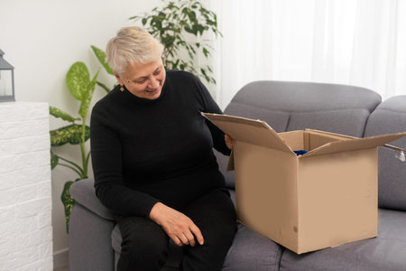 Elderly woman unpacking things in new house. opening cardboard box. Real estate, purchase concept