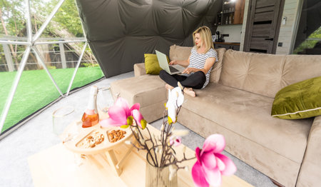 Transparent bubble tent at glamping, Lush forest around and interior. Woman with laptop
