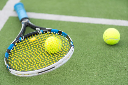 Tennis racket and tennis ball besides the net on outdoor tennis court.