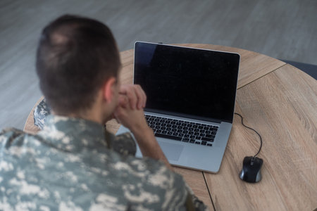 Young hispanic man army soldier using laptop sitting on table at home