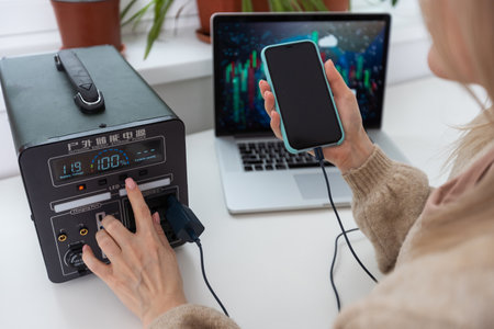 Woman inserting plug of portable solar station into socket at homeの写真素材