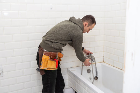 A male plumber with wrench repairs the faucet in the bathroom. replacement and maintenance of plumbing. handyman service. small business.の写真素材