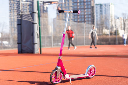 A small kids scooter stands on the sidewalk