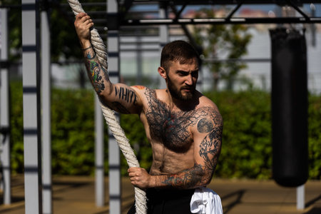 Muscular bodybuilder handsome man with naked torso trains triceps in a crossover cable exercise...