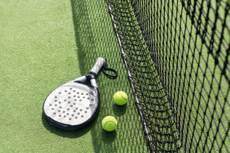 Padel racket and padel ball on a green court in the sunset
