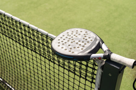 Padel racket and padel ball on a green court in the sunset