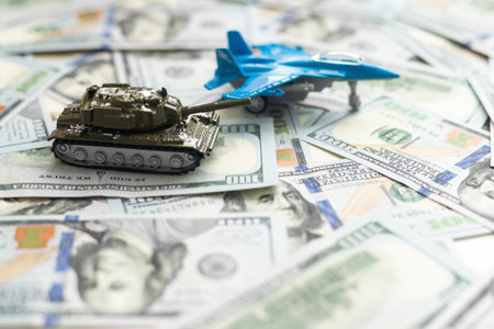 Toy tank on US hundred dollar bills banknotes close up. The concept of war costs, military spending...
