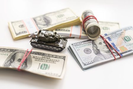 Toy tank on US hundred dollar bills banknotes close up. The concept of war costs, military spending...
