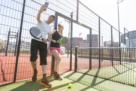 Portrait of positive young woman and adult man standing on padel tennis court, holding racket and...