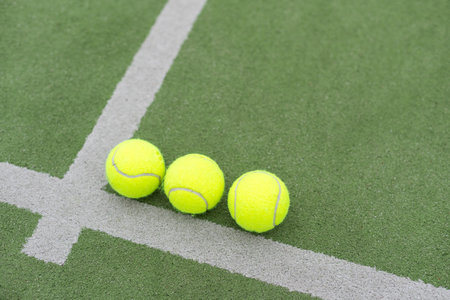 Yellow balls on grass turf near padel tennis racket behind net in green court outdoors with natural lighting. Paddle is a racquet game. Professional sport concept with copy space.の写真素材