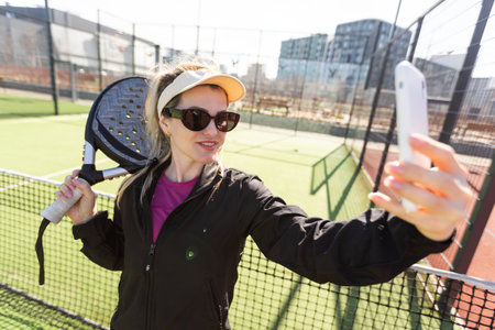 Young female smiling and looking at camera while playing padel against green backgroundの写真素材