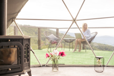 Hipster girl working with a laptop at home office in a glamping in the mountains with great views.の写真素材