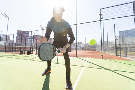 A padel player jump to the ball, good looking for posts and poster. Man with black racket playing a match in the open behind the net court outdoors. Professional sport concept with space for textの写真素材