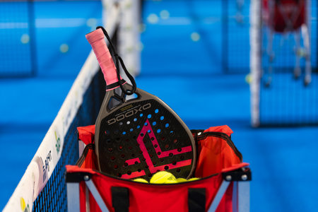 Kyiv, Ukraine, April 18, 2024. Black professional paddle tennis racket and ball with natural lighting on blue background. Horizontal sport theme poster, greeting cards, headers, website and appの写真素材