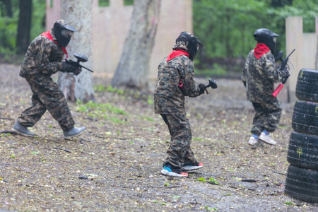Paintball game. Players with weapons shooting paint balls. Men on the playground. Guys in camouflage and masks are fighting.の写真素材