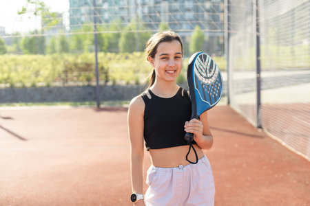 Teenage girl holding padel racquet in hand and ready to return ball while playing in court.の写真素材