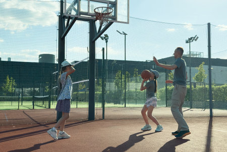 Father and teenage daughters playing basketball outside at courtの写真素材