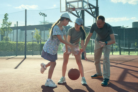a sports family plays basketball, father, daughters spend free time on the basketball court, lead a healthy lifestyle, a young girl throws a ball,の写真素材