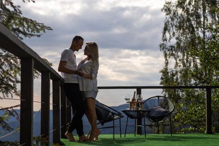 Horizontal sideview shot of a young couple in summer outfit enjoying the mountain view from terrace. Copy space.の写真素材