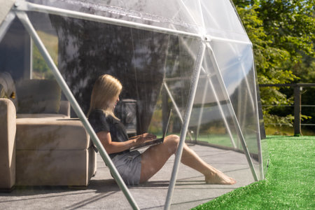 Young caucasian woman using and watching on laptop computer on in dome camping hotel. Tourism, vacation and weekend.の写真素材