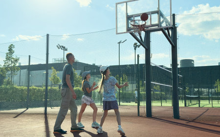 a sports family plays basketball, father, daughters spend free time on the basketball court, lead a healthy lifestyle, a young girl throws a ball,の写真素材