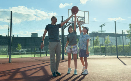 Father and teenage daughters playing basketball outside at court