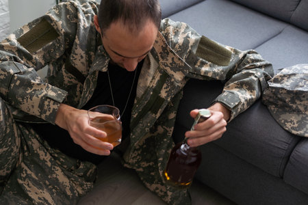 veteran holding bottle of whiskey near face while sitting in wheelchair with closed eyesの写真素材