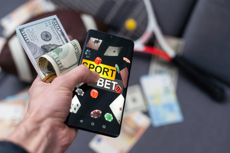 Online sports betting. Dollars are falling on the background of a hand with a smartphone and a soccer ball. Creative background, gamblingの写真素材