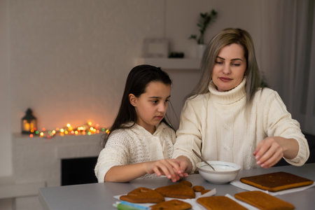 mother and daughter decorating gingerbread house. Beautiful living room with lights. Happy family celebrating holiday together.の写真素材