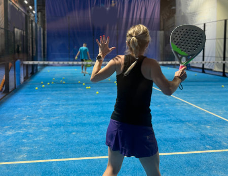 A woman is playing padel, hitting a ball on a bright blue court,の写真素材