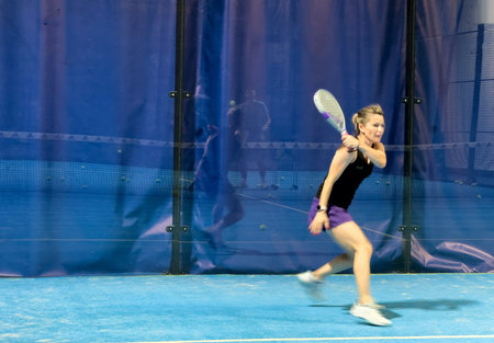 A woman is playing padel, hitting a ball on a bright blue court,の写真素材
