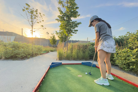 Mini Golf - girl playing Golf on green grass at sunset