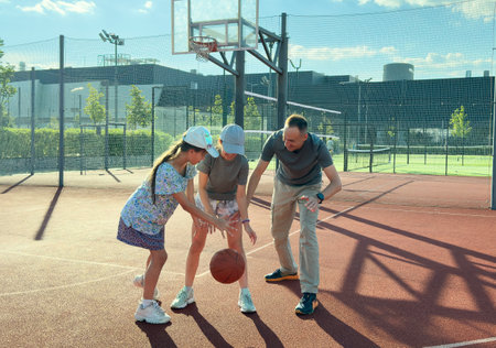 Father and teenage daughters playing basketball outside at courtの写真素材