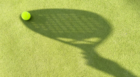 Shadow of a padel racket with a yellow ball on the green grass.の写真素材