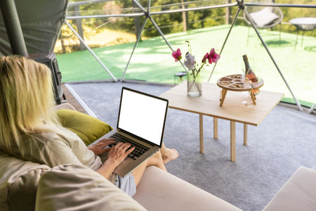 Young caucasian woman using and watching on laptop computer on in dome camping hotel. Tourism, vacation and weekend.の写真素材