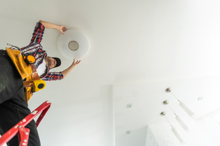 An electrician installs a ceiling light. Hands of an electrician installing and connecting a light to a ceiling.の写真素材