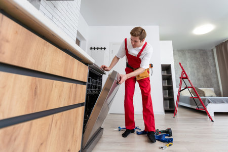 Full length of repairman repairing dishwasher with screwdriver in kitchen.の写真素材