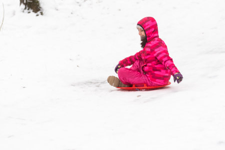 girl sliding down snowy hill with sledgeの写真素材