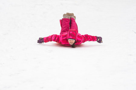 Pretty little girl wearing pink jacket and knitted hat walking in snowy winter park. Child playing with ice skating plate in forest. Family vacation with child in mountainsの写真素材