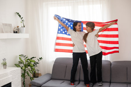 Brunette and blonde teenage girlfriends in white t-shirts holding american flag, energetic teenage friends spending time, friendshipの写真素材