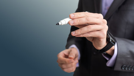 Man writes something on screen. Businessman raised his hand to screen. Concept - businessman writes on a virtual screen. Businessman held out a pen to camera. Guy in a suit on black background.の写真素材
