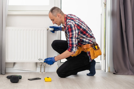 Close-up Of A Young Male Plumber Installing Radiator With Screwdriverの写真素材