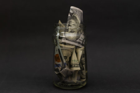 Many 100 US dollars bank notes in a glass jar isolatedの写真素材