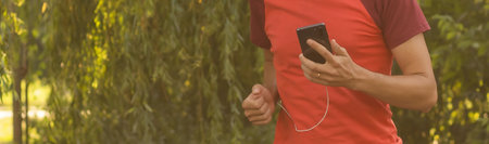 A handsome man in a T-shirt trains in the park and listens to music on headphonesの写真素材