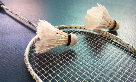Cream white badminton shuttlecock and racket with neon light shading on floor in indoor badminton court, copy space, soft and selective focus.の写真素材