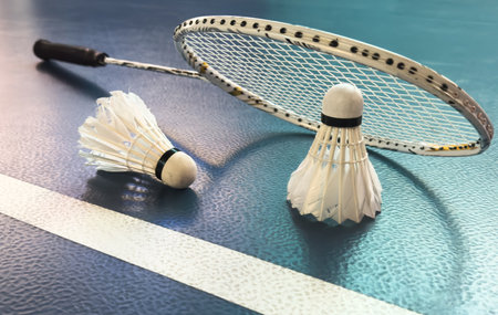 Cream white badminton shuttlecock and racket with neon light shading on floor in indoor badminton court, copy space, soft and selective focus.の写真素材