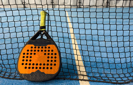 Black professional paddle tennis racket and ball with natural lighting on blue background. Horizontal sport theme poster, greeting cards, headers, website and appの写真素材